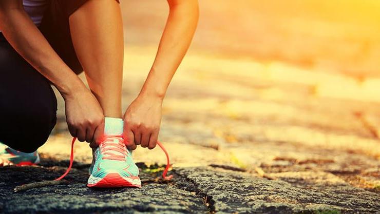 Woman tying workout sneaker outdoors at sunrise or sunset